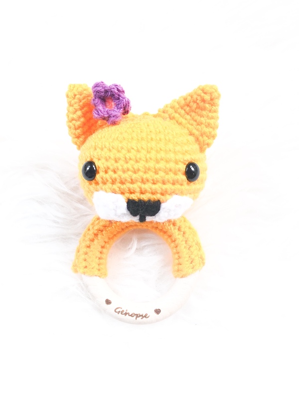 Gehäkelter orange‑weißer Fuchs‑Greifling mit lila Blüte an einem Holzring.