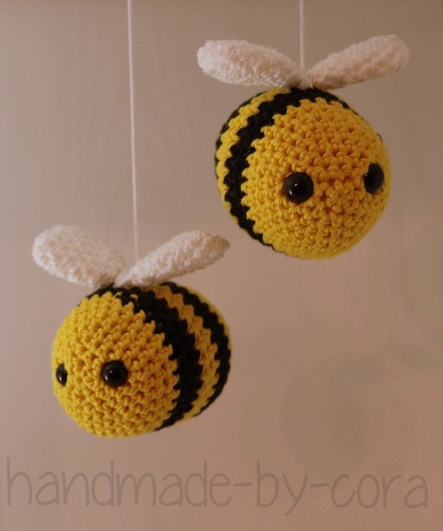Zwei gehäkelte Bienen-Amigurumi mit weißen Flügeln, an feinen Fäden hängend