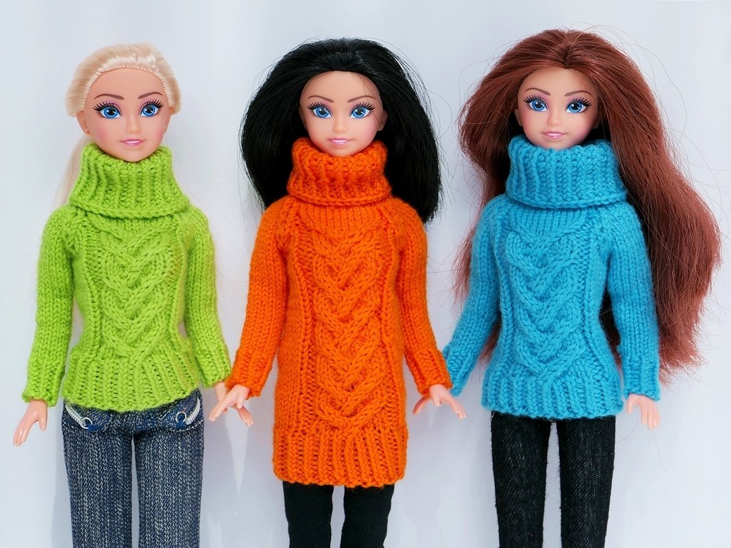 Drei Puppen in gestrickten Rollkragenpullovern mit Zopfmuster in Grün, Orange und Türkis