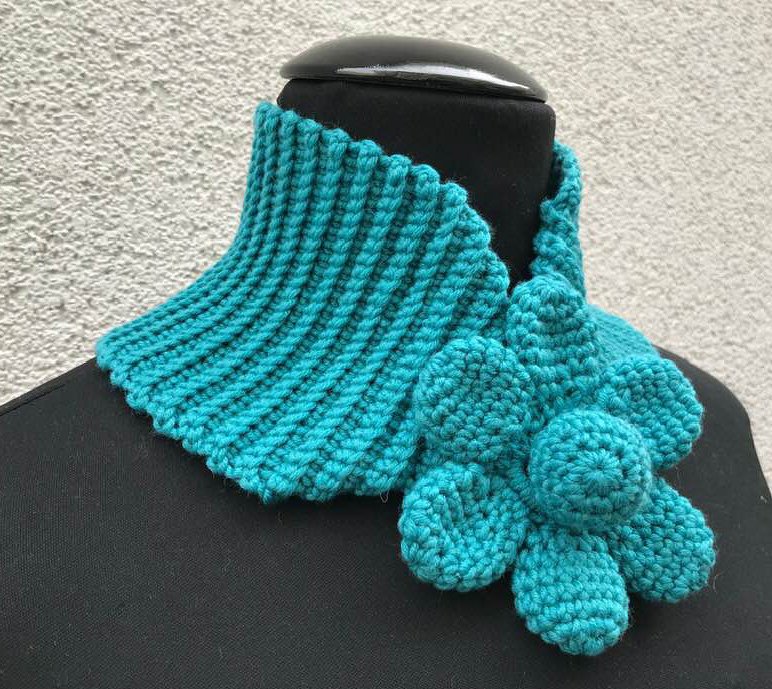 Türkisfarbener gehäkelter Kragenschal mit geripptem Kragen und großer Blüte an einer schwarzen Schaufensterpuppe.