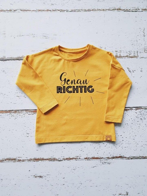 Gelbes Kinder-Langarmshirt mit schwarzem Schriftzug 'Genau Richtig' und radialen Strahlen