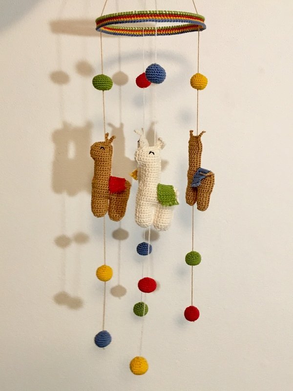Gehäkeltes Mobile mit drei Lama-Figuren und bunten Häkelkugeln an einem regenbogenfarbenen Ring.