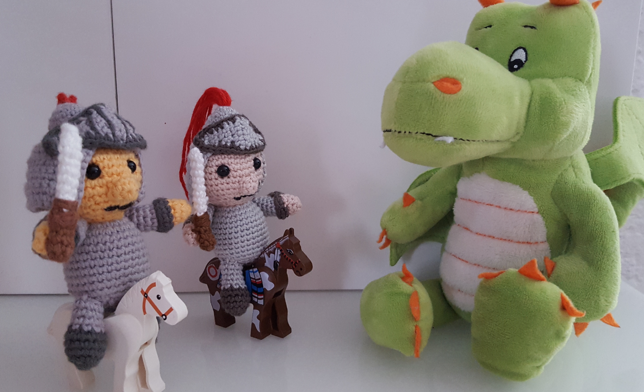 Zwei Amigurumi‑Ritter auf Spielpferden neben grünem Plüschdrachen