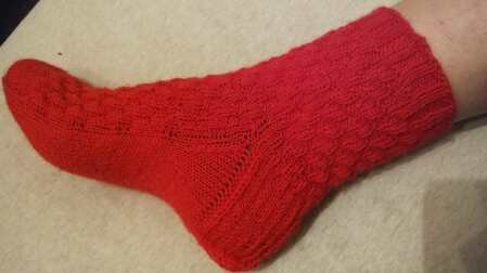 Rote gestrickte Socke mit sichtbarem Relief- und Strukturmuster an einem Fuß
