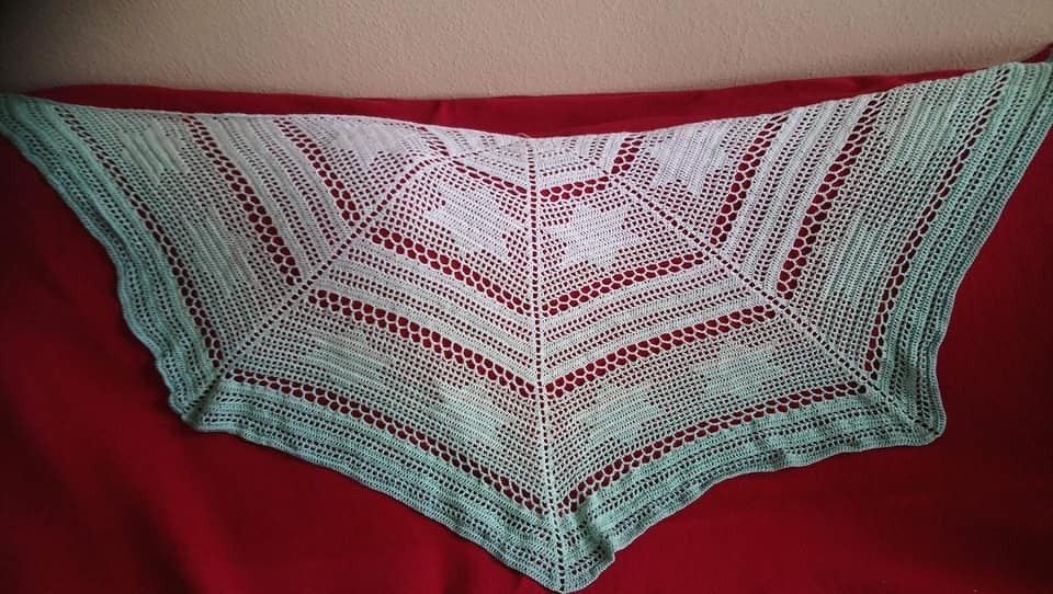 Halbrund gehäkeltes Tuch in Pastellgrün mit Lochreihen und Herzmotiven auf rotem Hintergrund