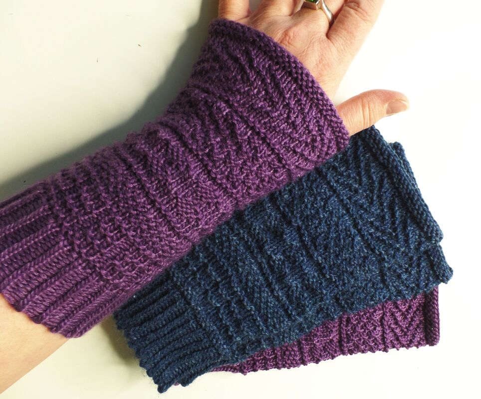 Zwei gestrickte Armstulpen in Lila und Dunkelblau, eine am Handgelenk getragen, mit Rippenmuster.