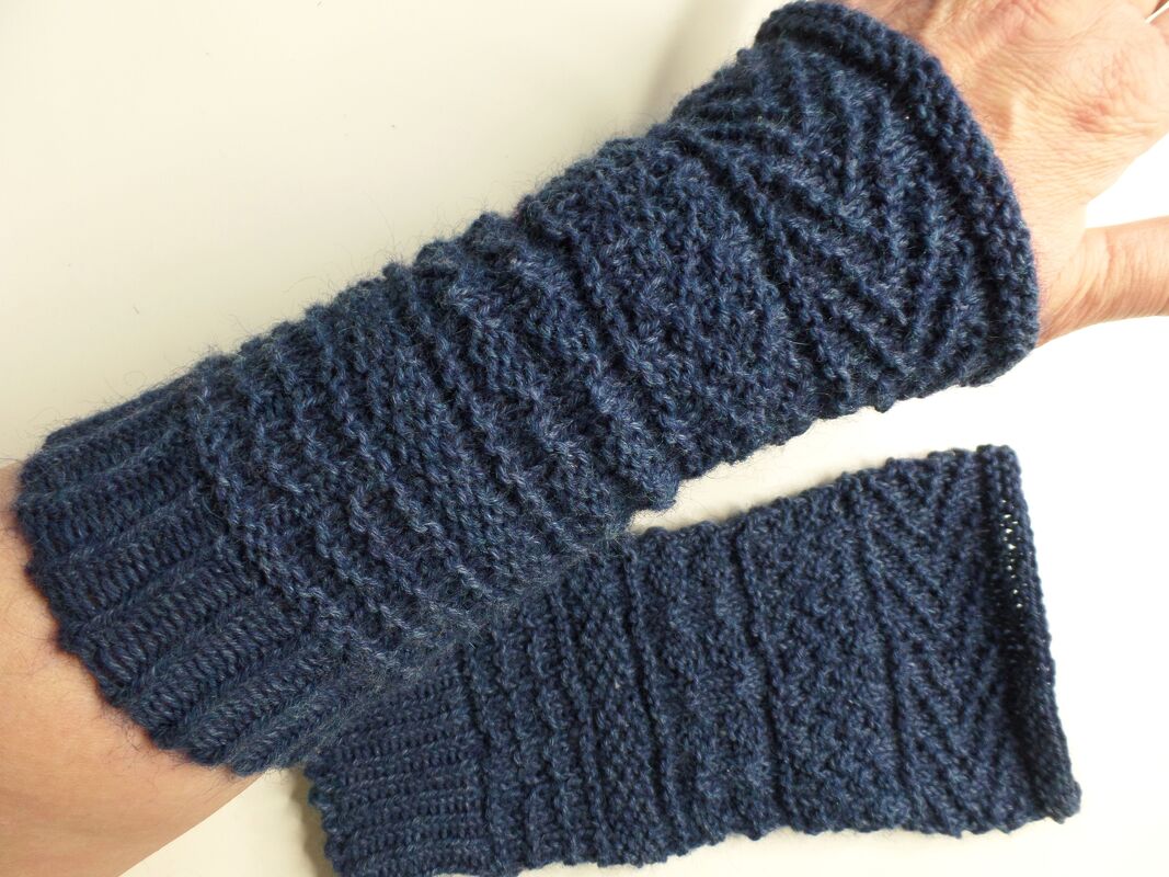 Dunkelblaue, gestrickte Armstulpen mit diagonalem Rippenmuster, eine am Unterarm getragen, die zweite daneben liegend