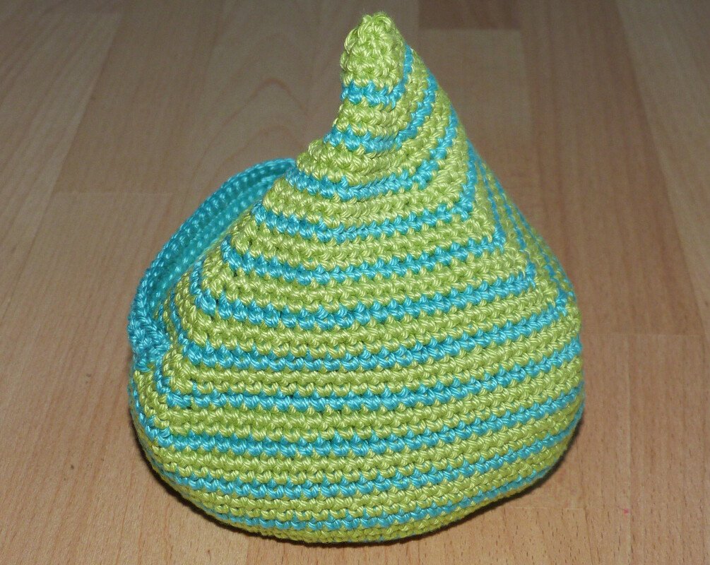 Gehäkeltes konisches Objekt mit hellgrünen und türkisen Streifen auf Holzuntergrund