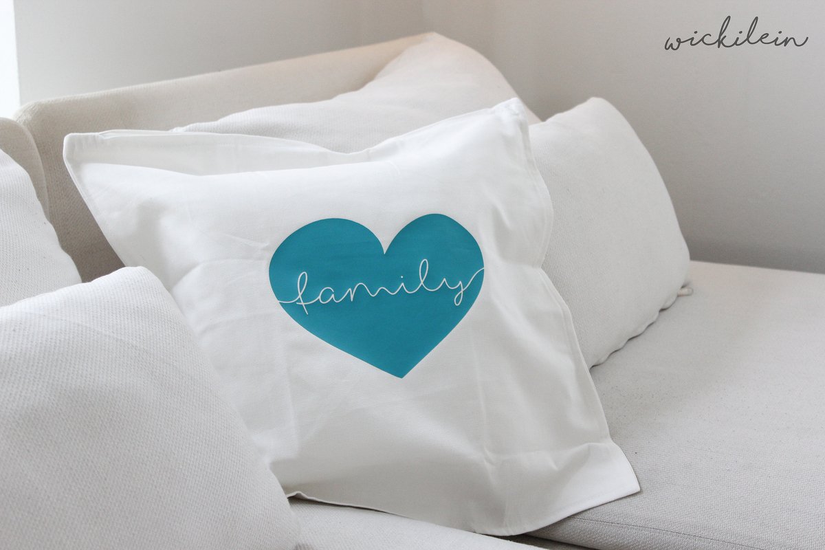 Weißes Dekokissen mit türkisblauem Herz und handschriftlichem 'family' Schriftzug