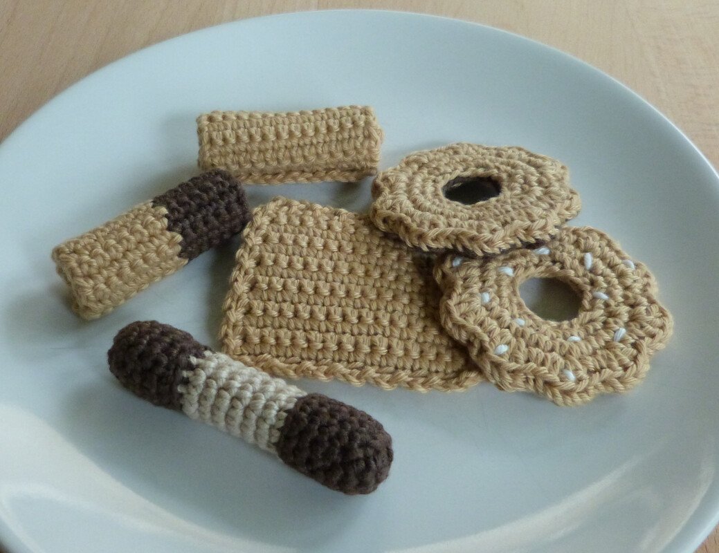 Verschiedene schnell gehäkelte Spielkekse und Riegel aus Garn auf weißem Teller