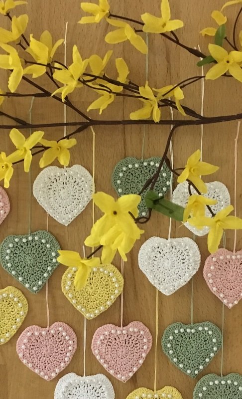 Gehäkelte Pastellherzen mit Perlen an gelben Forsythienzweigen