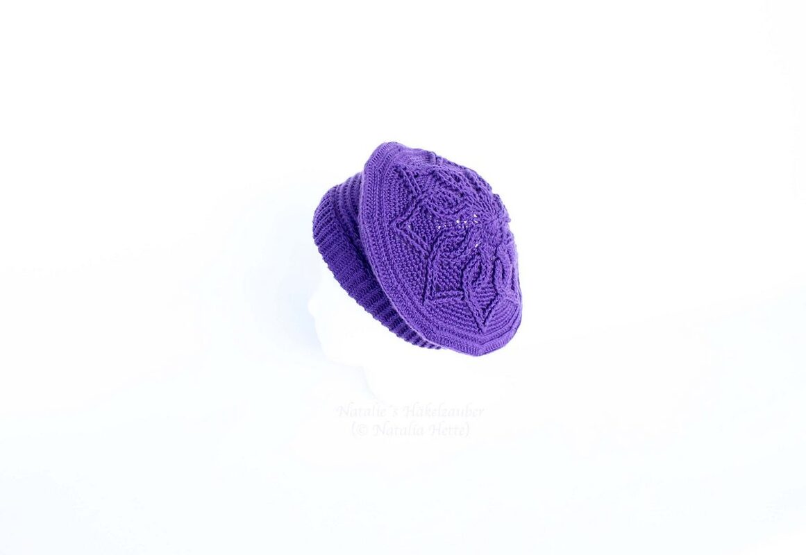 Purple crocheted beanie with detailed textured stitch pattern and ribbed edge on a white background.
