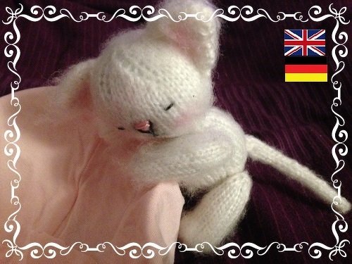 Close-up of a cream knitted amigurumi kitten with closed eyes on pink cloth
