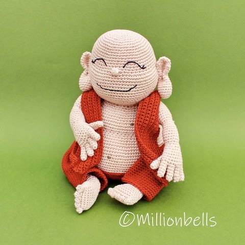 Gehäkelte Amigurumi-Figur in Creme mit orangefarbener Weste, sitzend auf grünem Hintergrund