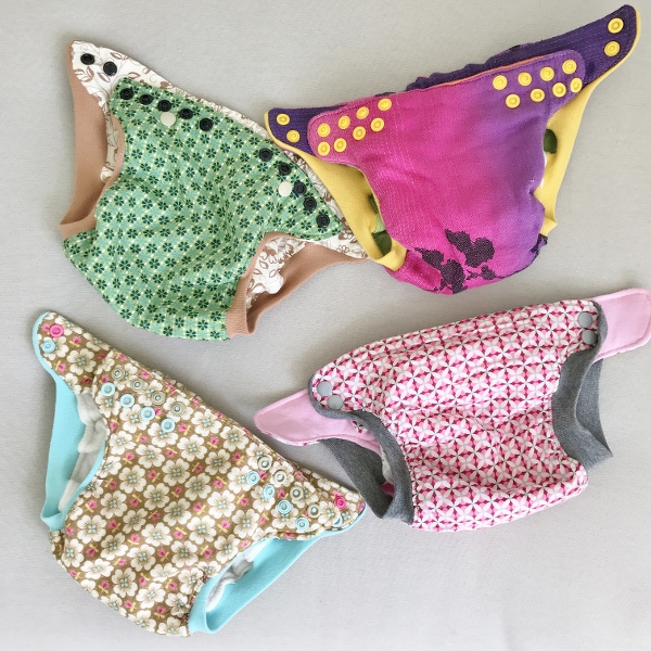 Vier bunte, gemusterte Stoff-Windelüberhosen mit farbigen Druckknöpfen und elastischen Beinbündchen