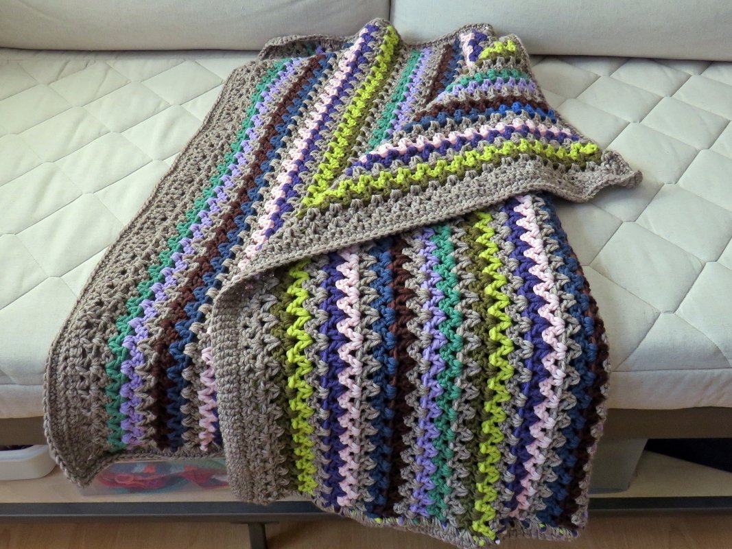 Bunte gehäkelte Decke mit Wellenmuster auf hellem Sofa