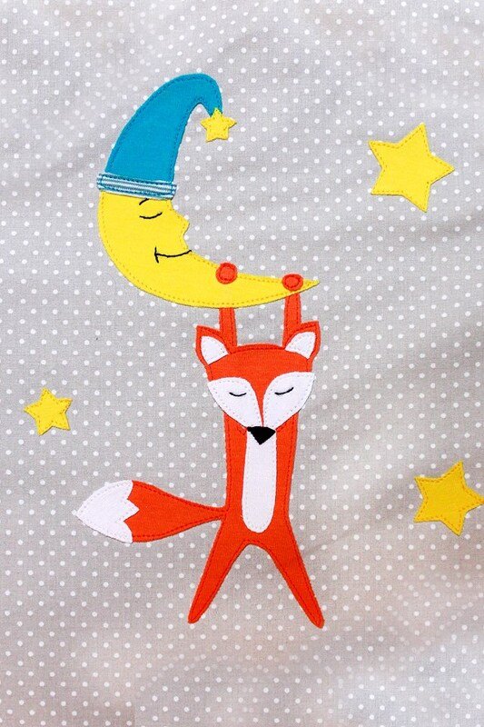 Applikation: Fuchs hält einen gelben Halbmond mit Schlafmütze, umgeben von Sternen, auf hellgrauem Stoff mit weißen Punkten.