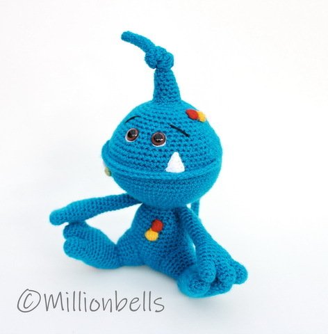 Blue crocheted amigurumi monster seated, with a twisted horn, two small white teeth and round brown eyes
