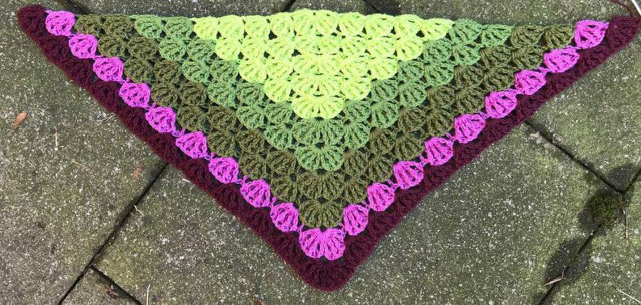 Gehäkeltes Dreieckstuch in Hellgrün, Oliv und Burgunder mit magenta Muschelmuster-Bordüre auf grauem Pflaster