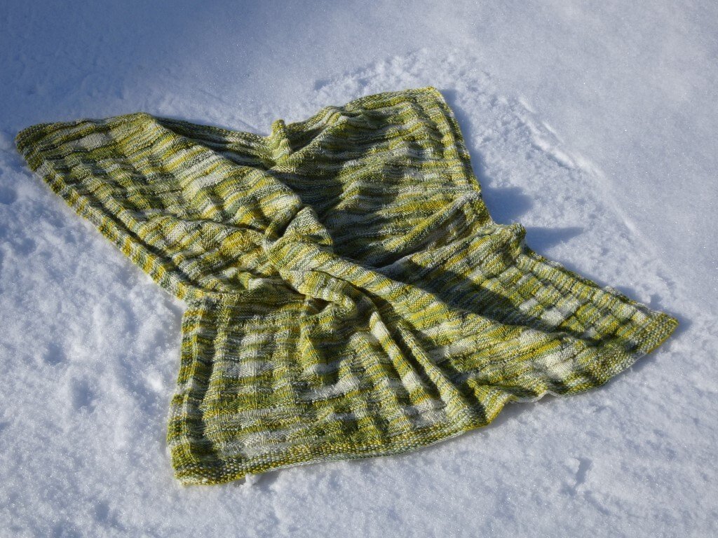 Gestrickte Babydecke in Grüntönen mit Streifen liegt auf Schnee