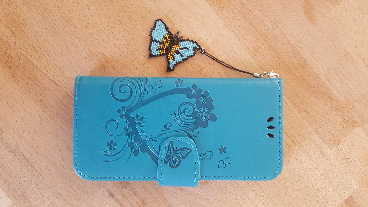 Perlen-Schmetterlingsanhänger an einer türkisfarbenen Klapphülle mit floraler Prägung