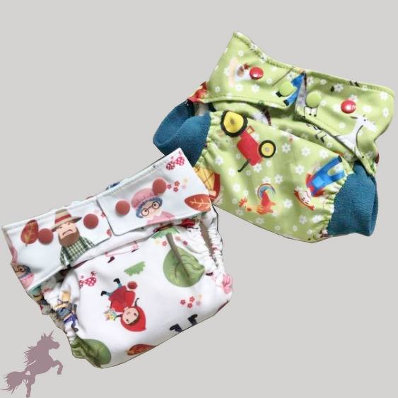 Zwei bunte Stoffwindeln, eine grün mit Traktor und Bauernhoftieren, eine weiß mit Märchenmotiven.