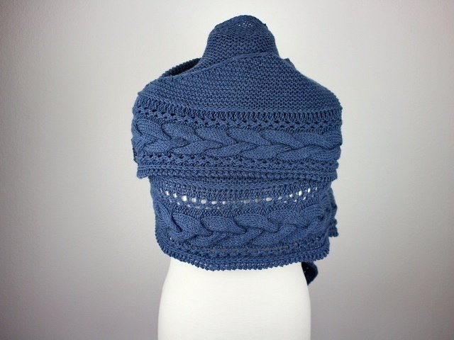 Knitted blue crescent shawl with prominent cable and eyelet patterns displayed on a mannequin