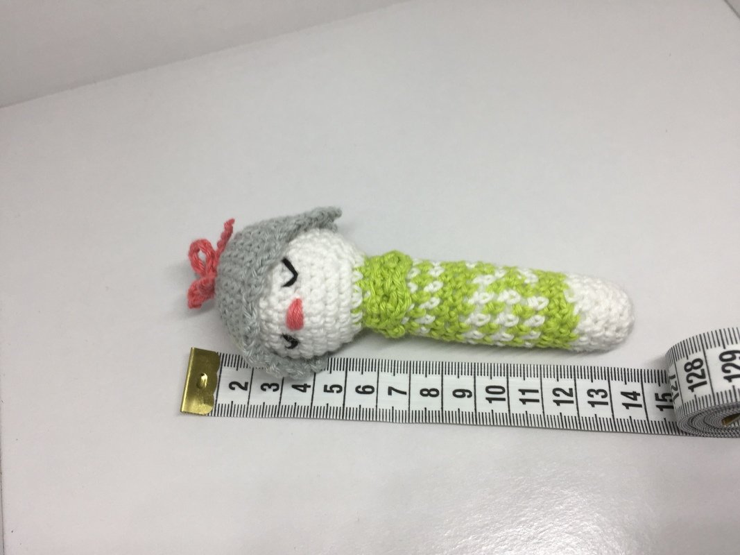 Handgehäkelte Baby-Rassel mit grauer Mütze, grün-weißem Griff und Maßband