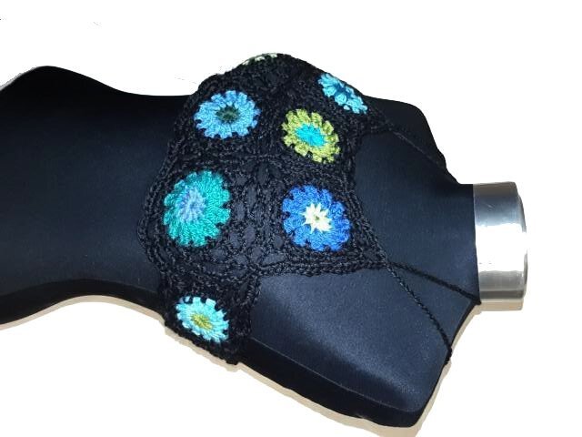 Gehäkeltes schwarzes Crop-Top mit blauen und grünen Blumen-Granny-Squares auf schwarzer Büste.