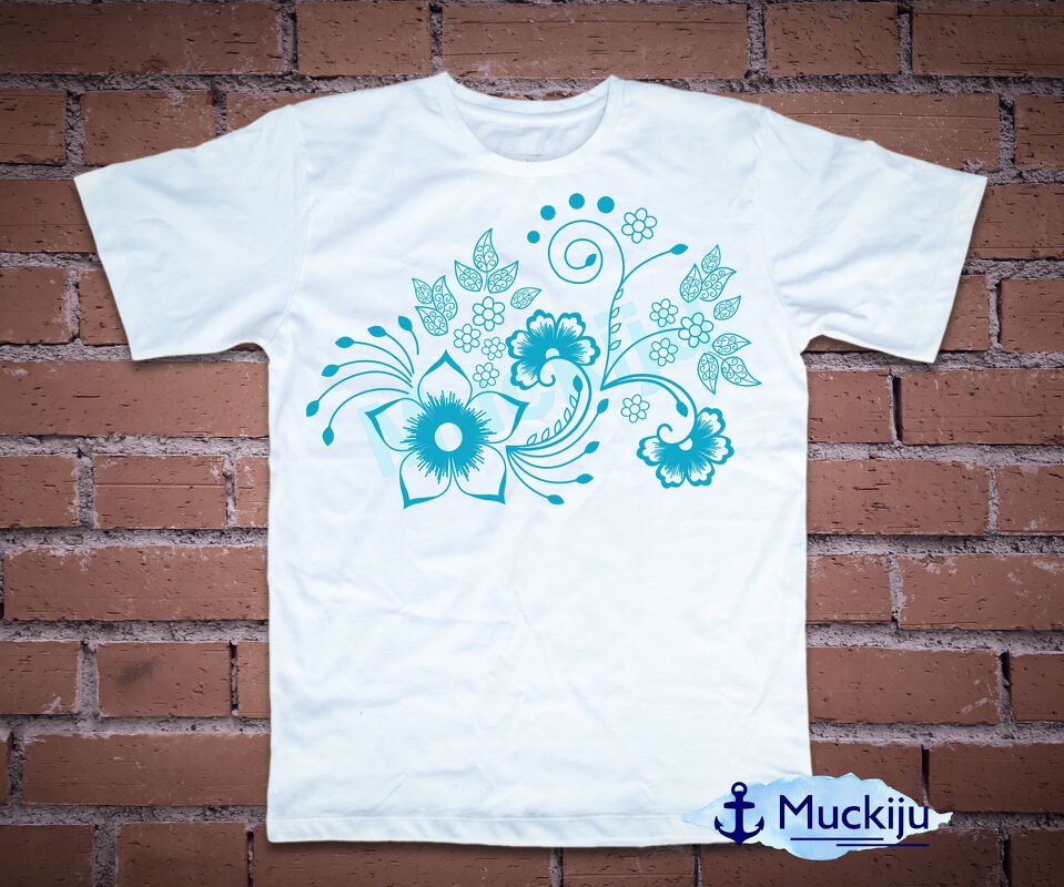 Weißes T-Shirt mit türkisem Blumenmuster vor einer Ziegelwand.