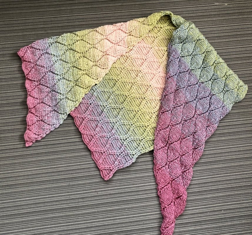Gehäkeltes Dreieckstuch mit diamantförmigem Relief und rosa‑grünem Farbverlauf auf neutralem Untergrund