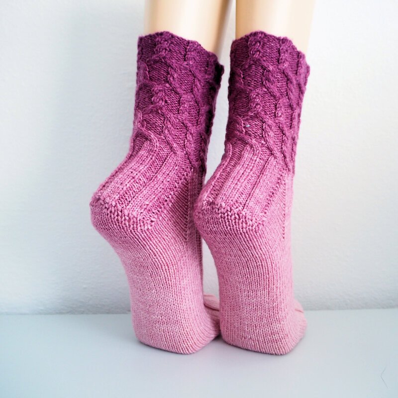 Close-up of pink to purple ombre knitted socks with cable cuff and ribbed ankle.
