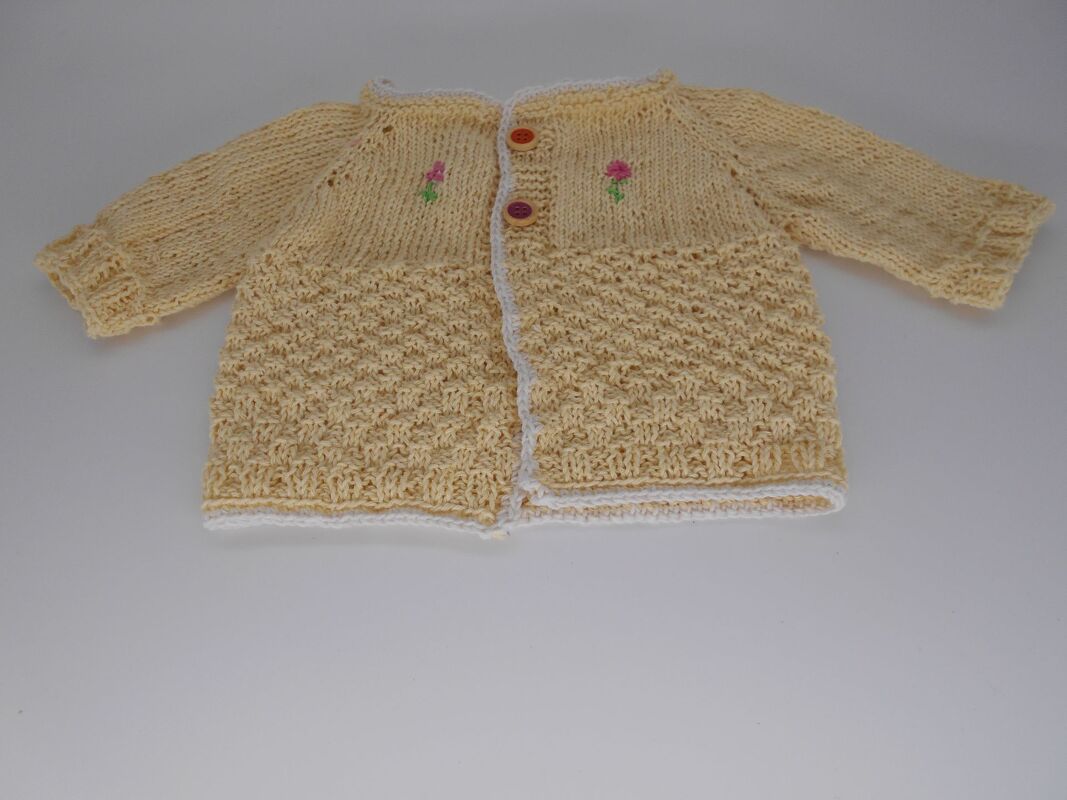 Gelbe handgestrickte Babyjacke mit rosa Blumenstickerei, Knöpfen und weißer Einfassung, flach liegend.