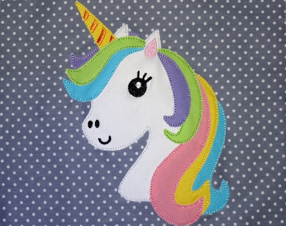 Verspieltes Einhorn-Stickmotiv mit pastellfarbener Mähne auf gepunktetem Stoff