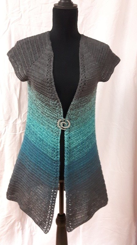 Gehäkelte Damenweste Grau‑Türkis auf Schneiderpuppe, kurze Ärmel, offene Vorderseite mit Zierschließe