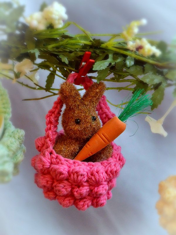 Gehäkelter brauner Hase mit Karotte in rosafarbenem Körbchen, hängend an einem Zweig