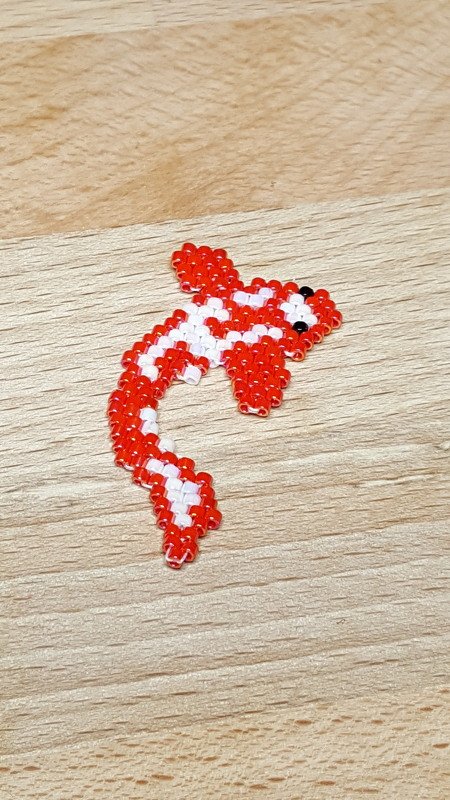 Kleiner Koi aus roten und weißen Rocailles-Perlen mit schwarzem Auge auf hellem Holz