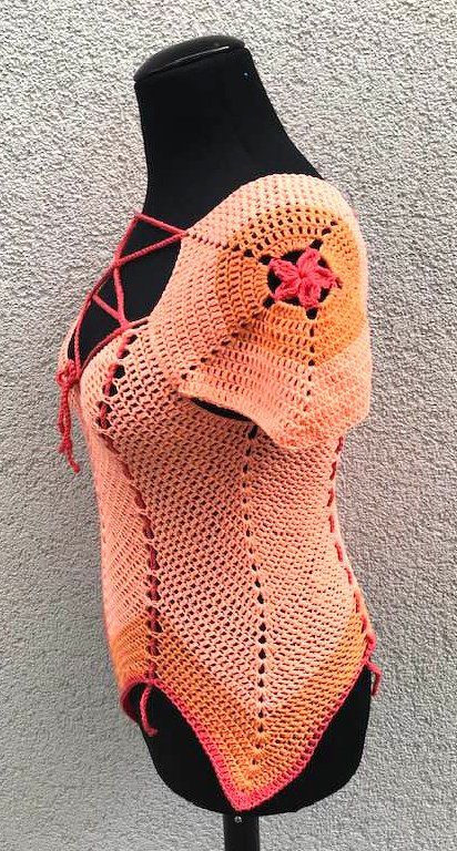 Gehäkeltes schulterfreies Damen-Top in Pfirsich/Orange mit Schnürung und Blumenmotiv auf schwarzer Schaufensterpuppe.