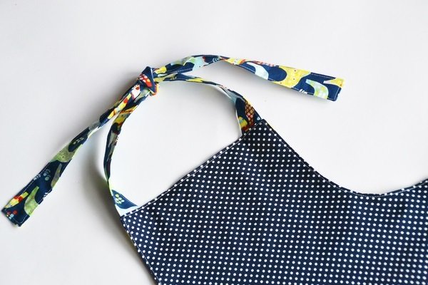 Nahaufnahme: dunkelblauer Stoff mit weißen Pünktchen und buntem Bindeband mit Tiermotiven, geknotet.