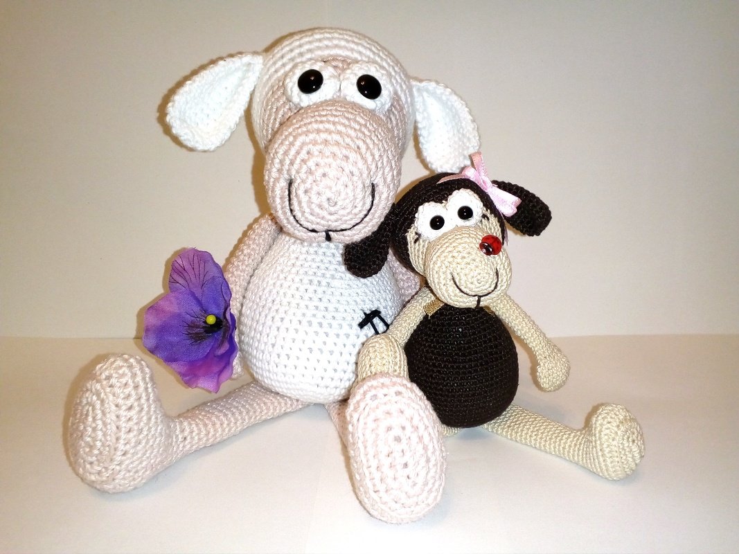 Zwei gehäkelte Amigurumi: helles Schaf mit violetter Blume und kleiner Hund mit rosa Schleife