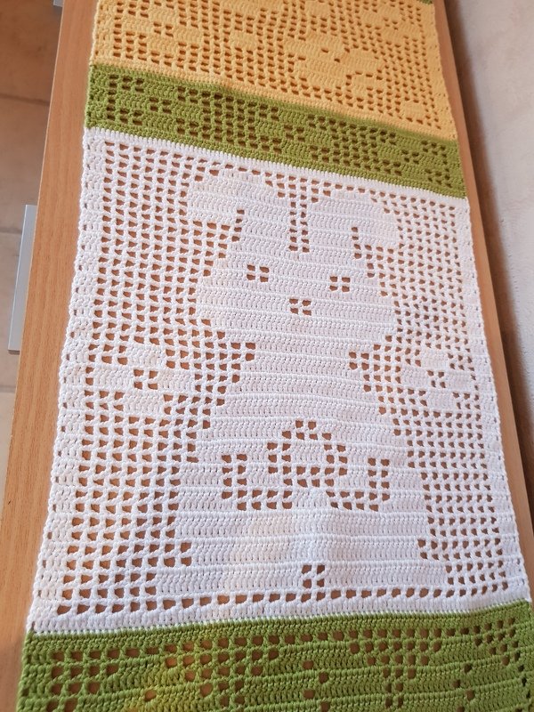 Filethäkel-Tischläufer mit durchbrochenem Hasenmotiv und gelb-grünen Randstreifen auf Holztisch