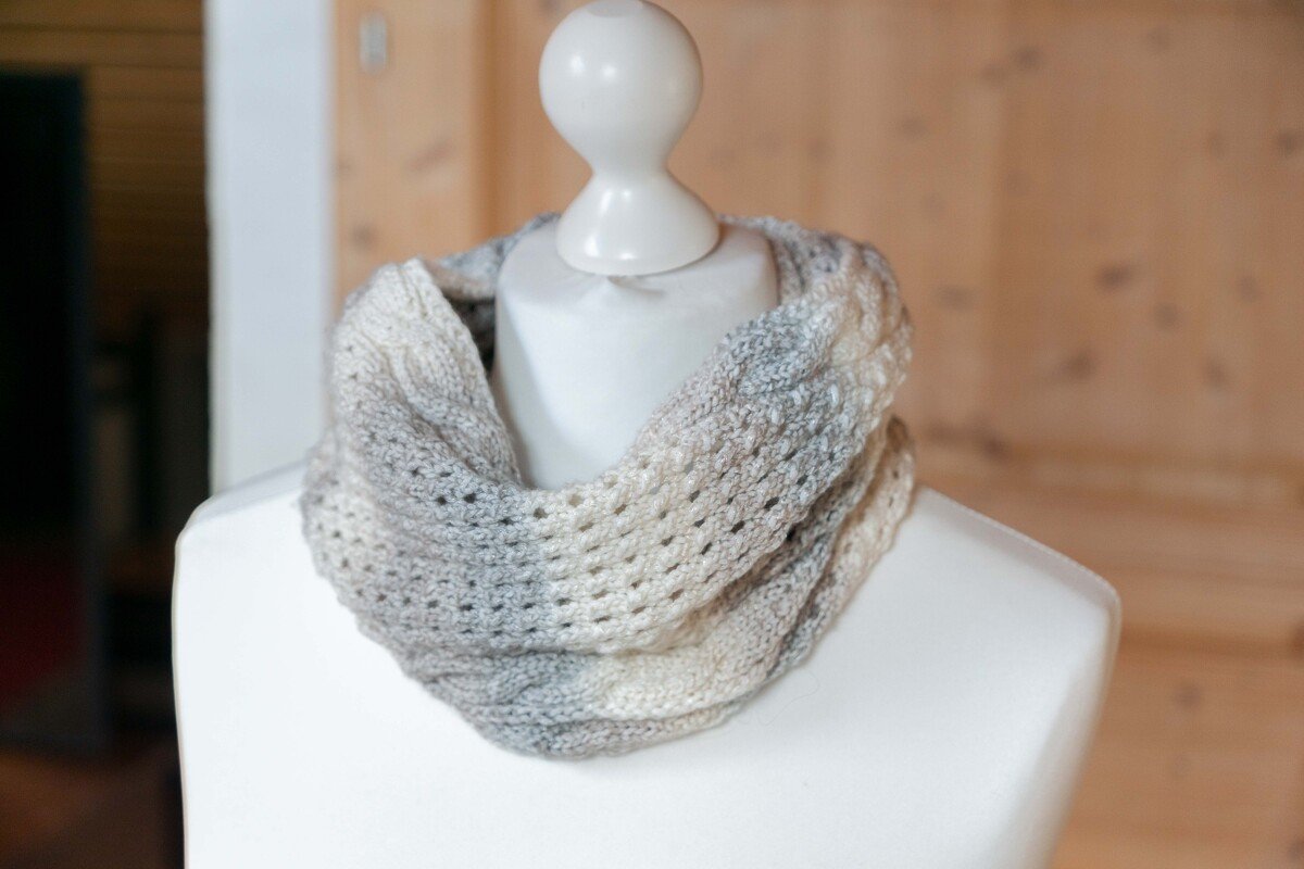 Gestrickter Loop‑Schal in Grau‑Beige‑Ombré mit Lochmuster auf einer weißen Schaufensterpuppe