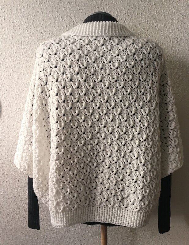 Rückansicht eines weißen gehäkelten Seelenwärmers auf einem Mannequin mit Lochmuster und Rippenbündchen