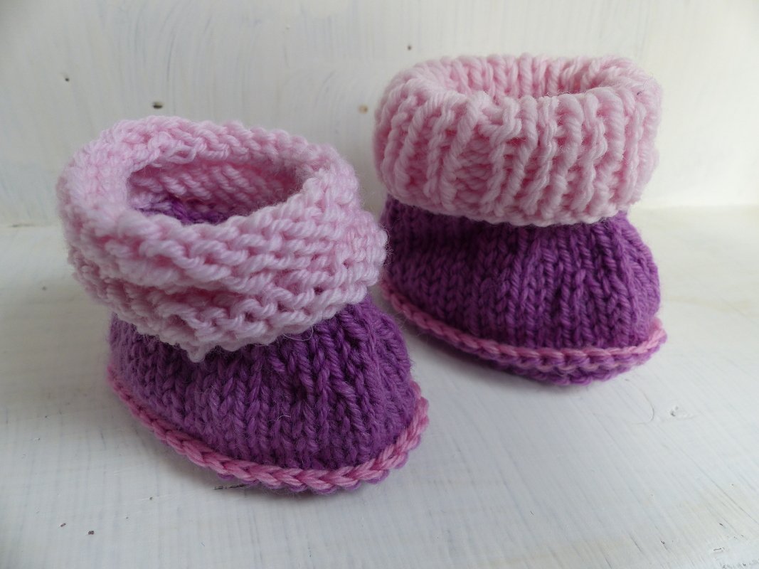 Zwei gestrickte Babyschühchen in Lila und Rosa auf hellem Untergrund