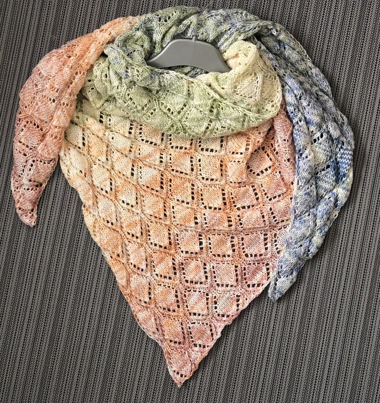 Gestricktes Dreieckstuch in Pfirsich-, Grün- und Blautönen mit rautenförmigem Lochmuster, an einem Bügel aufgehängt