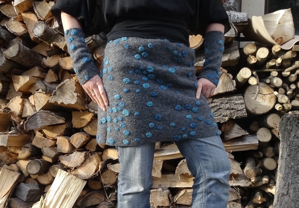 Grauer Filzrock mit türkisfarbenen Punkten und passende Armstulpen vor gestapeltem Brennholz