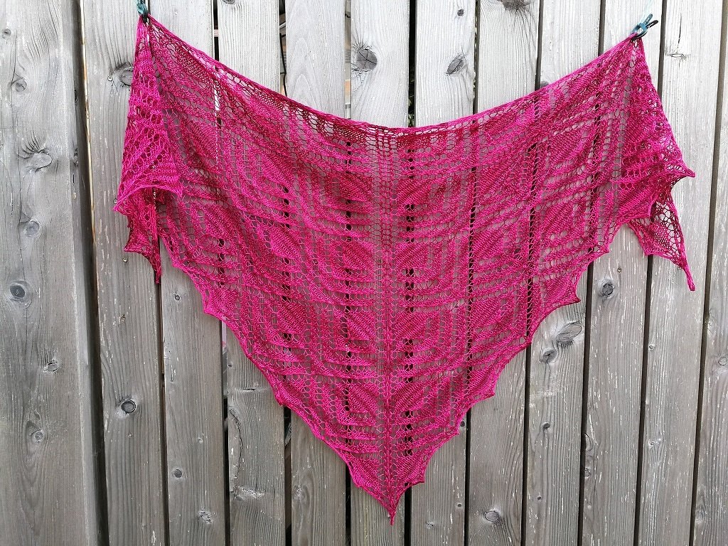 Gestricktes pinkes Dreieckslacetuch mit Blatt- und Rankenmuster am Holzzaun befestigt