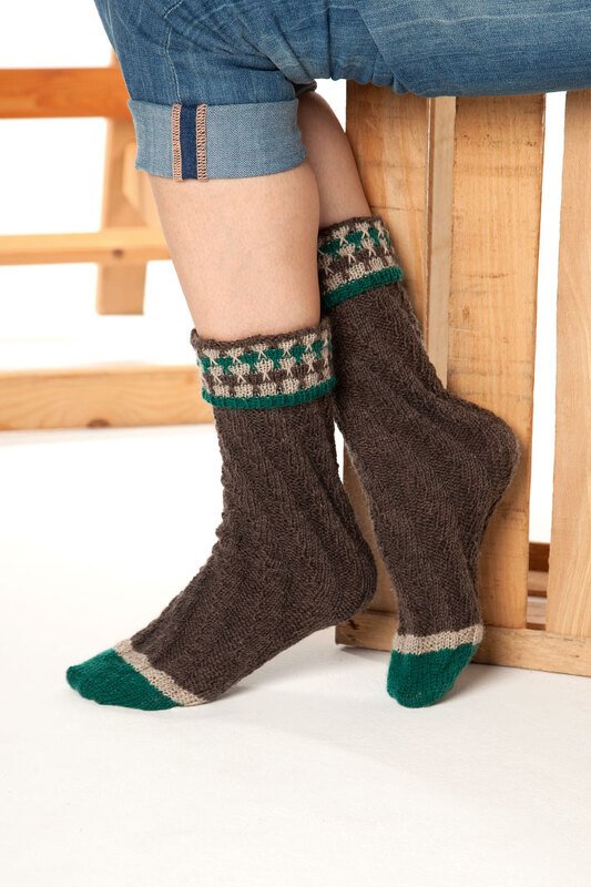 Dunkelbraune gestrickte Socken mit grün-cremefarbenem Rautenmuster am Umschlagbündchen und grünen Zehen, getragen zu Jeans.