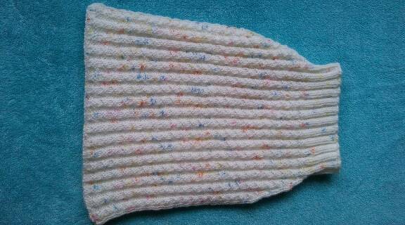 Gestrickter cremefarbener Babysack mit bunten Sprenkeln und Rippenmuster auf blauem Stoff