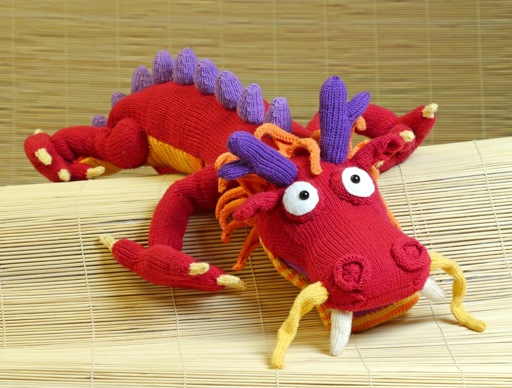 Gestrickter roter Drache mit lila Stacheln und gelbem Bauch auf einer Bambusmatte
